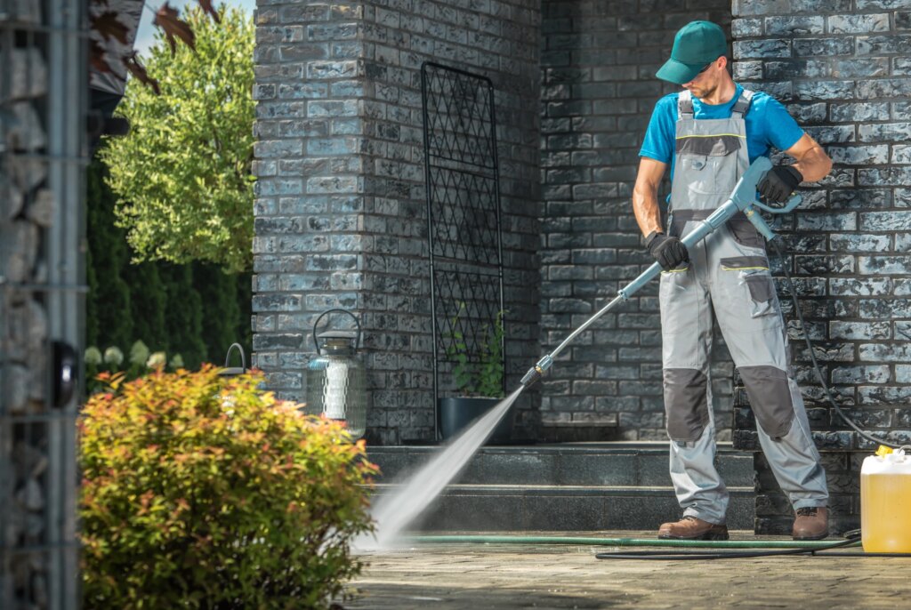 Driveway Pressure Washing. Male Worker Cleaning Area in Front of the House.